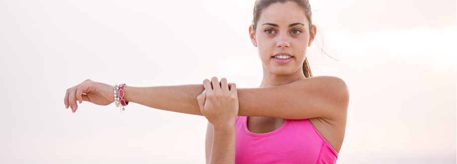 young brunette woman wearing pink workout top, stretching arm