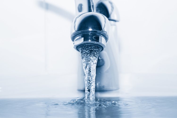 Closeup of a gray-blue silver bathroom faucet running and wasting water