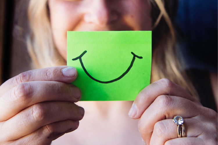 woman holding a green paper smile in front of her face