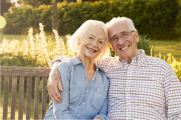 senior couple sitting on a bench outside pondering the benefits of a fixed bridge vs dentures for tooth loss