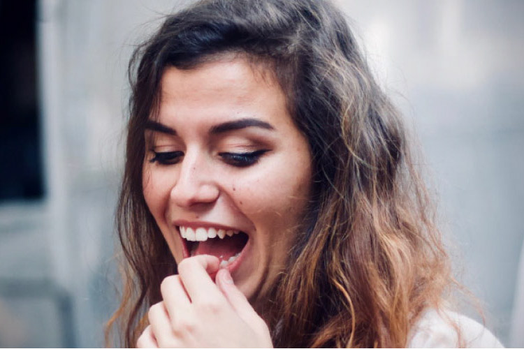 dark haired girl holding a painful cracked tooth in her mouth