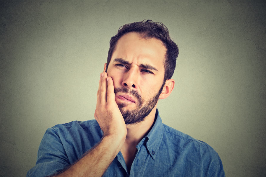 bearded man holds his jaw in pain from swollen gums