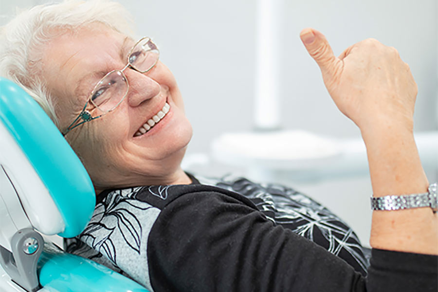 senior woman sitting in the dentist chair gives a thumbs up after getting a dental bridge