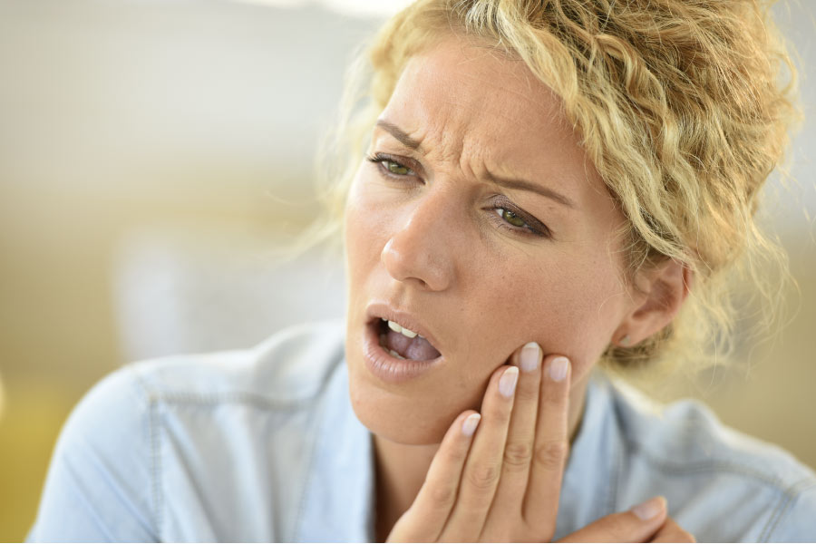 blond woman holds her jaw in pain with TMJ disorder