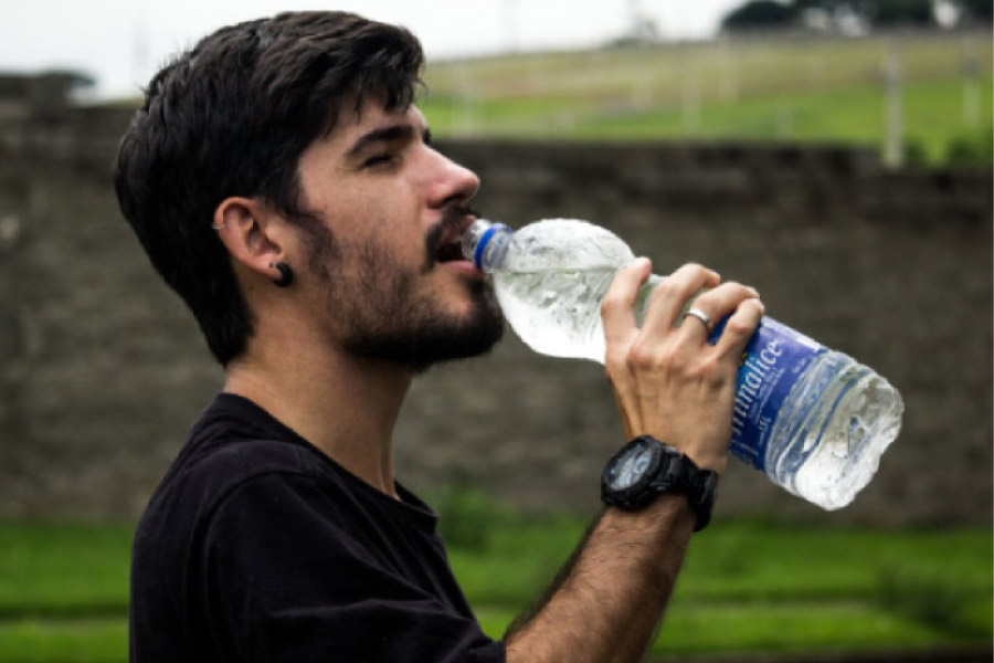 man drinks out of a big water bottle, generating saliva to help his oral health