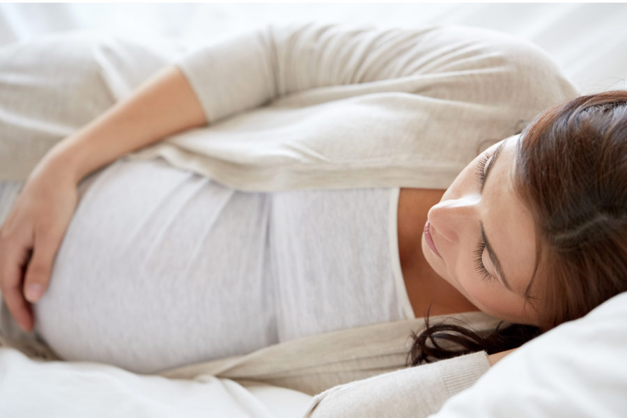 Pregnant woman lies on her side holding her belly